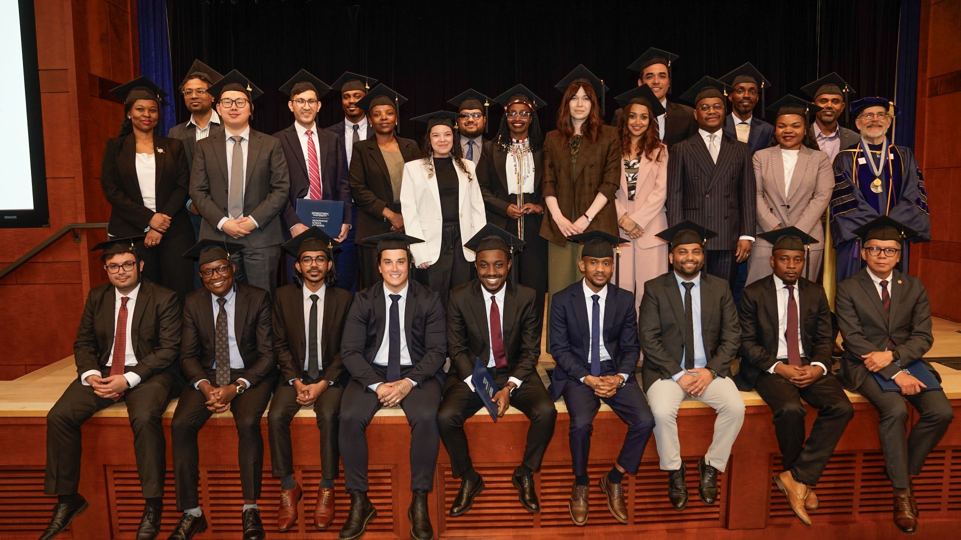 Large group of business professionals in formal attire posed in rows on stage